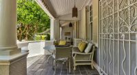 A secluded and inviting patio space at Parker Cottage featuring comfortable outdoor seating adorned with vibrant yellow and patterned cushions, all shaded by a classic white porch.