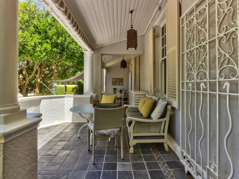 A secluded and inviting patio space at Parker Cottage featuring comfortable outdoor seating adorned with vibrant yellow and patterned cushions, all shaded by a classic white porch.